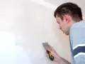 Uomo con spatola ripara una crepa su un muro bianco.