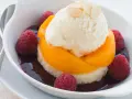 Ein köstlicher Pfirsich Melba: Vanilleeis auf Pfirsichspalten, umgeben von Himbeeren und dunkler Sauce, garniert mit Mandelblättchen.