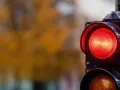 Close-up of a red traffic light with a blurred background of autumn foliage.