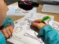 Dziecko koloruje edukacyjne karty pracy z dinozaurem i artefaktami.