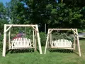 Two wooden porch swings stand on a grassy lawn, surrounded by colorful flowers and lush trees. This image offers inspiration for how to hang a porch swing.