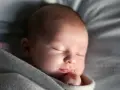 Śpiący noworodek otulony kocykiem. Zastanawiasz się, jak szybko rosną noworodki? Ten maluch to dowód, że dzieje się to w mgnieniu oka.