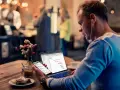 Hombre revisa datos de business intelligence hostelería en su laptop y móvil, sentado en una cafetería.