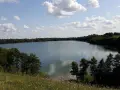 Spokojne jezioro Hańcza otoczone zielonymi lasami, z białymi chmurami na błękitnym niebie.
