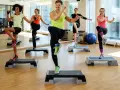 En grupp människor utför step ups i ett gym. De har roligt medan de tränar.
