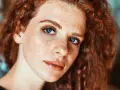 Primo piano di una ragazza con lentiggini e capelli rossi, con un trucco naturale che esalta la sua bellezza.
