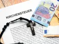 Kirchensteuer-Dokument mit Kreuz und Euro-Scheinen. Lohnt sich Kirchenaustritt finanziell? Die Dokumente und Geldscheine deuten auf eine finanzielle Entscheidung hin.