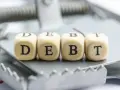 Cztery drewniane kostki z literami D, E, B, T tworzą słowo "DEBT" na pułapce. To symbol finansowych zobowiązań, które mogą prowadzić do trudnej sytuacji, jak datio in solutum.