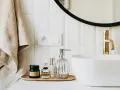 Sur un plateau en bois, des flacons de parfum et un distributeur de savon argenté. Une serviette beige est suspendue à côté d'un lavabo blanc et d'un robinet doré. La colle carrelage flex, c'est quoi ?