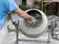 Mieszanie betonu w betoniarce. Pracownik w rękawicach sprawdza konsystencję, zastanawiając się, ile cementu na metr sześcienny betonu potrzeba do uzyskania idealnej mieszanki.