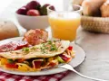 Pyszne śniadanie bez chleba: omlet z warzywami i serem, bekon, pomidory, truskawki i sok pomarańczowy.