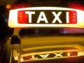 Leuchtendes TAXI-Schild mit roten Blinklichtern, das einen Taxi-Alarm signalisiert. Die Reflexion auf dem dunklen Auto verstärkt die nächtliche Atmosphäre.