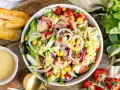 Ein bunter gemischter Salat mit knackigem Salat, Tomaten, Gurken, Mais und roten Zwiebeln, serviert mit Dressing und geröstetem Brot.