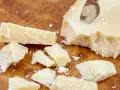 Kawałki sera Grana Padano na drewnianej desce. Czy Grana Padano to parmezan? Ten twardy ser dojrzewa długo, podobnie jak parmezan.