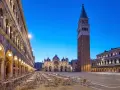 Piazza San Marco a Venezia, con la Basilica e il Campanile, testimoni della ricca storia della città. Tavolini all'aperto creano un'atmosfera serale.