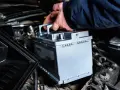 Mano che inserisce una nuova batteria. La batteria della macchina serve per avviare il motore e alimentare i sistemi elettrici.