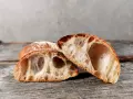 Zwei Hälften eines rustikalen ciabatta mit sauerteig, mit großer, luftiger Krume und knuspriger Kruste, liegen auf einem Holzbrett.