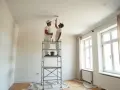 Deux peintres sur un échafaudage peignent un plafond. Ils se demandent combien de temps pour peindre un plafond de 50m2.