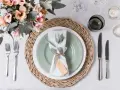 Une table dressée avec une assiette verte, une serviette blanche décorée d'une branche d'eucalyptus et d'une étiquette, le tout sur un rond de serviette fait maison.