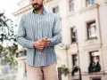 Mężczyzna w paski koszuli, z rękami złożonymi na brzuchu, idealnie pokazuje, kiedy koszula w spodnie tworzy elegancki look.