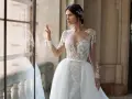 Panna młoda w sukni ślubnej z koronką i trenem, z ozdobną fryzurą w stylu bollywood, patrzy przez okno.