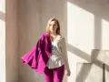 Młoda kobieta w białej koszuli i spodniach, na ramieniu zarzucony marynarka w intensywnym, **magenta kolorze**.