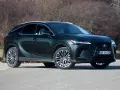 Ciemnozielony Lexus 450h z eleganckimi felgami stoi na drodze, otoczony suchymi krzewami.