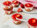 Mehrere kleine Gläser mit einem cremigen Dessert mit Erdbeeren und einer roten Erdbeersauce.