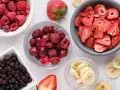 Miseczki pełne liofilizowanych malin, truskawek, wiśni, borówek i bananów.