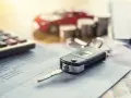 Autoschlüssel liegt auf einem Kontoauszug. Im Hintergrund ein rotes Spielzeugauto, Münzen und ein Taschenrechner. TSN VSN.