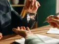 Przekazanie kluczy do nowego domu po podpisaniu umowy przedwstępnej. Dwie osoby przy biurku, jedna podaje klucze, druga trzyma długopis nad dokumentem.