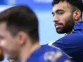 Hassan Kaddah, z brodą i kręconymi włosami, w niebieskiej bluzie z żółtymi detalami, spogląda w bok.