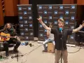 Un groupe rock alternatif français en pleine performance, avec un guitariste, un percussionniste et un chanteur énergique.