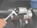 A hand uses a hammer to tap a car's starter motor, a common trick for how to start a car with a bad starter.