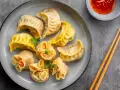 Talerz pełen aromatycznych chińskich pierożków, gotowych do zanurzenia w sosie. Obok pałeczki i miseczka z ostrym dipem.