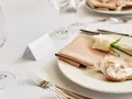 Elegancko nakryty stół weselny z różową serwetką, białą różą i pierniczkiem. Idealne miejsce na zastanowienie, jakie wino na wesele wybrać.