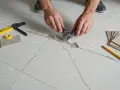 Inspection d'une fissure dans le chape avant la pose du carrelage. Outils de mesure et échantillons de carreaux à proximité.