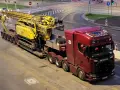 Czerwona ciężarówka Scania z przyczepą transportuje żółtą maszynę wiertniczą. Pilot pojazdu nienormatywnego czeka na przejazd.
