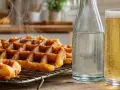 Gaufres croustillantes fumantes sur une grille, accompagnées d'une bouteille d'eau pétillante et d'un verre de bière dorée. Parfait pour une recette de gaufres croustillantes.