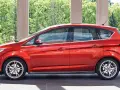 Czerwony Ford C-Max 1.6 benzyna zaparkowany pod arkadami, z zielenią w tle.