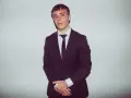 Młody mężczyzna w czarnym garniturze i białej koszuli, z krawatem. Kinny Zimner prezentuje się elegancko.