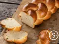 Ein goldbraunes Zopf Brot, frisch gebacken, liegt auf Backpapier. Zwei Scheiben sind abgetrennt und zeigen die weiche Krume.