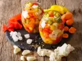 Due barattoli di giardiniera fatta in casa, pieni di verdure colorate come peperoni, carote e cavolfiore, su un tagliere di ardesia con ingredienti freschi intorno.