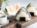Trójkątne onigiri sushi z czarnym sezamem i kawałkiem nori na drewnianej desce.