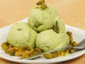 Tre palline di cremoso gelato al pistacchio, guarnite con pistacchi interi, su un piatto bianco con una spolverata di pistacchi tostati.