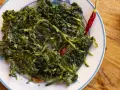 Un piatto di cicoria in padella, condita con peperoncino rosso e un filo d'olio d'oliva, su un tavolo di legno.