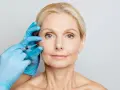 Zabieg z użyciem botoksu, czy botox jest bezpieczny? Dłoń w niebieskiej rękawiczce wykonuje zastrzyk w okolicę oka kobiety.