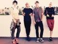 Gwen Stefani und ihre Bandkollegen posieren lässig vor einer Kulisse mit Palmen.