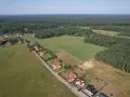 Widok z lotu ptaka na wieś otoczoną lasem. Widać domy z czerwonymi dachami, pola uprawne i jezioro. Każdy dom zajmuje swój kawałek ziemi, a całość tworzy malowniczy krajobraz.