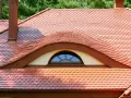 Dachówki ceramiczne w kolorze ceglastym pokrywają dach z charakterystycznym lukarną w kształcie oka.